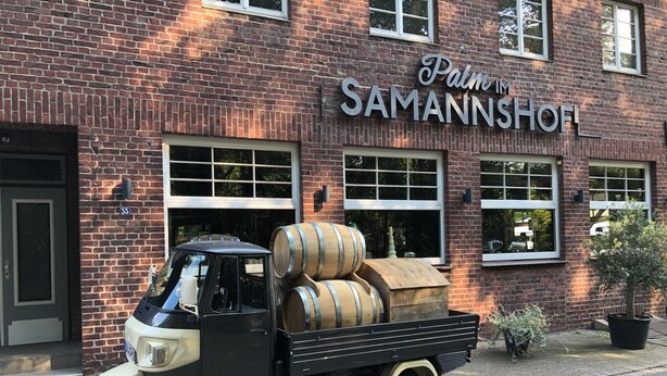 Un camión antiguo estacionado frente a un edificio de ladrillo con un letrero que dice 'Palm Samannshof'.