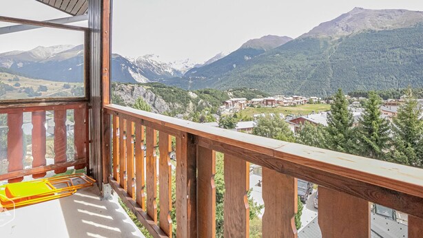 Een balkon met houten hekwerk met uitzicht op een bergachtig landschap met gebouwen in de vallei.