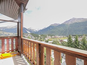 Een balkon met houten hekwerk met uitzicht op een bergachtig landschap met gebouwen in de vallei.