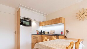 A compact kitchen with wooden cabinets, a built-in oven, and a dining area with a table and chairs. - Charming Savoyard apartment for 5 with parking (Aussois)