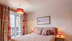 A bedroom with a bed, two bedside tables, a window with curtains, a hanging light fixture, and a framed picture on the wall. - Charming Savoyard apartment for 5 with parking (Aussois)