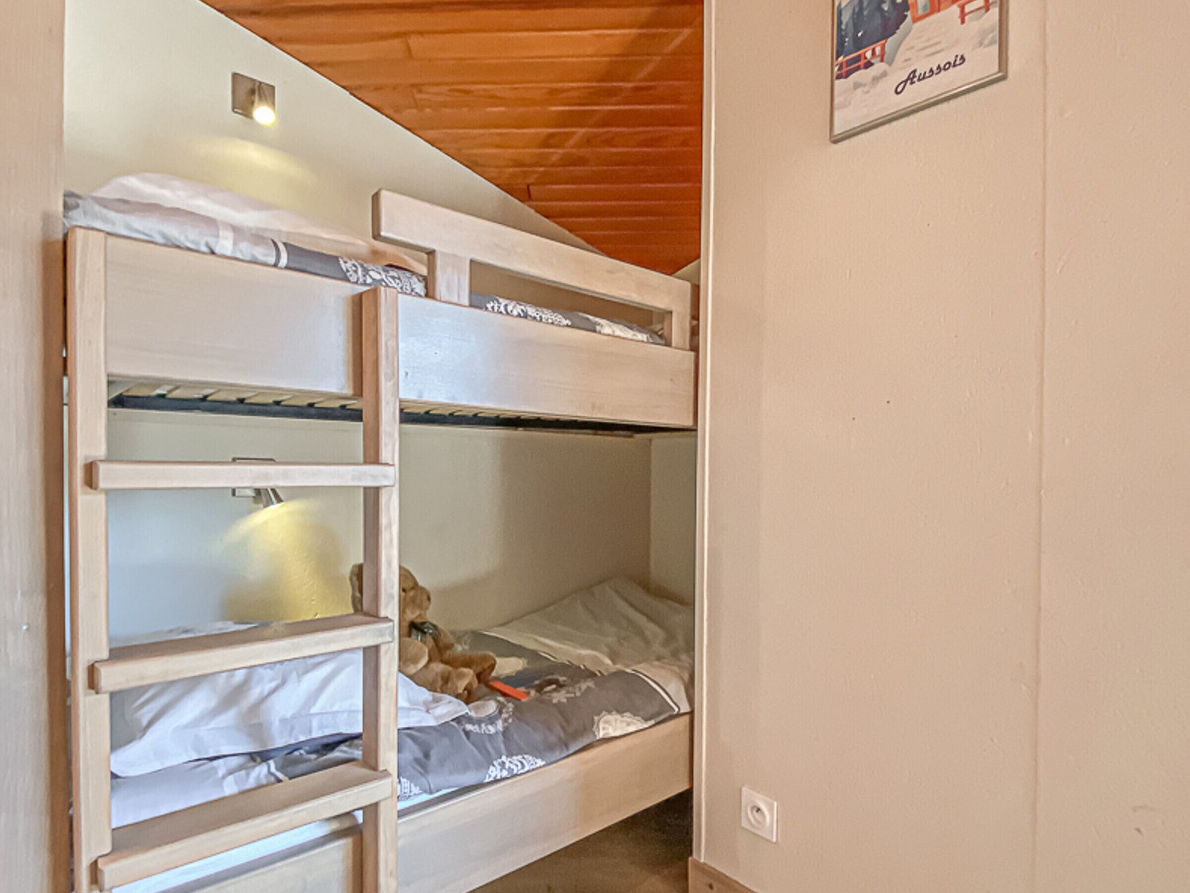 Een stapelbed met een ladder, een teddybeer en een poster aan de muur.