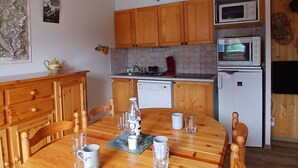 A compact kitchen with wooden cabinets, a microwave, a refrigerator, and a dining table set for four. - Cozy apartment near leisure, 6 people, Wifi (Aussois)