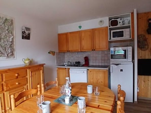Eine kompakte Küche mit Holzausstattung, einer Mikrowelle, einem Kühlschrank und einem Esstisch für vier Personen.