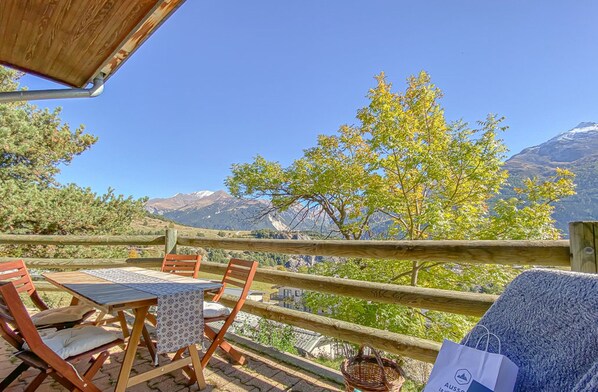 Un terrazzo in legno con tavolo e sedie, affacciato su un paesaggio montuoso.