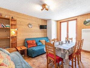 A cozy room with a wooden wall, a blue sofa, a dining table with chairs, a bookshelf, and a television. - Apartment with sunny terrace, pets allowed, parking included (Aussois)