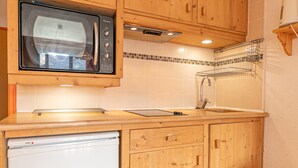 Une cuisine compacte avec des meubles en bois, un four à micro-ondes, un évier et un petit réfrigérateur.