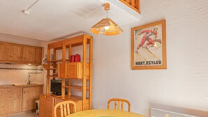 Une cuisine avec des meubles de rangement en bois, une table à manger avec des chaises, un luminaire suspendu et un tableau encadré au mur.
