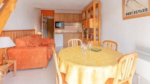 Une pièce chaleureuse comprenant une table à manger, un canapé orange, des meubles en bois et un coin cuisine équipé d’un four à micro-ondes.