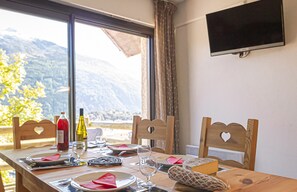 Una mesa de comedor servida con platos, vasos y cubiertos, una botella de vino y una tabla de quesos.