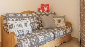 A cozy room with a wooden sofa, patterned cushions, a framed picture on the wall, and a red gift bag. - Aussois: 2-room apartment, terrace, sleeps 6, pets allowed, WIFI (Aussois)