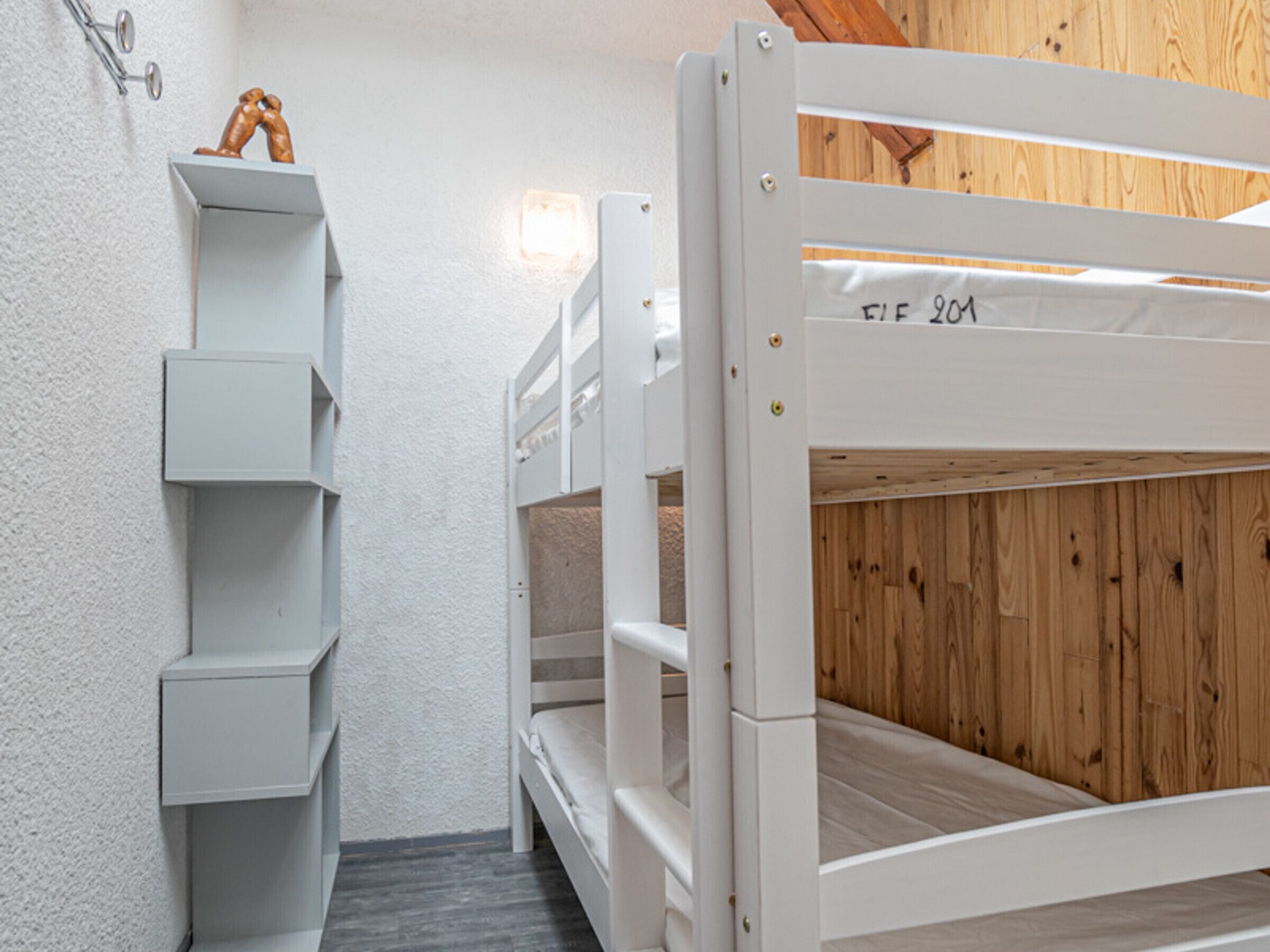 Una cama litera con cabecera de madera y una pared blanca con estanterías.