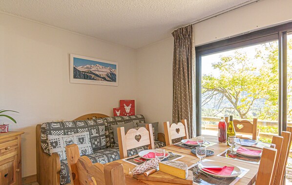 A dining area with a table set for four, a sofa, and a window with a view of trees. - 2-room Apartment in Aussois - 6 people, WIFI, pets allowed (Aussois)