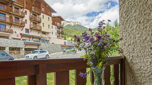 Un balcon offrant une vue dégagée sur une montagne, une clôture en bois et un vase rempli de fleurs.