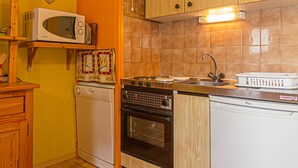 Une cuisine de taille réduite, dotée de meubles en bois, d’un four à micro-ondes, d’une cuisinière et d’un lave-vaisselle.