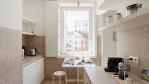 Una cocina moderna con ventana, armarios blancos, cafetera y comedor.