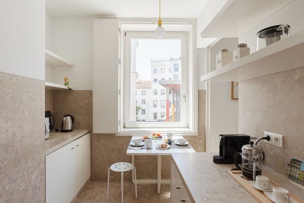 A modern kitchen with a window, white cabinets, a coffee maker, and a dining area.