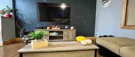A living room with a flat-screen TV, a wooden coffee table, a sofa, decorative pumpkins, and a wall with a star pattern.