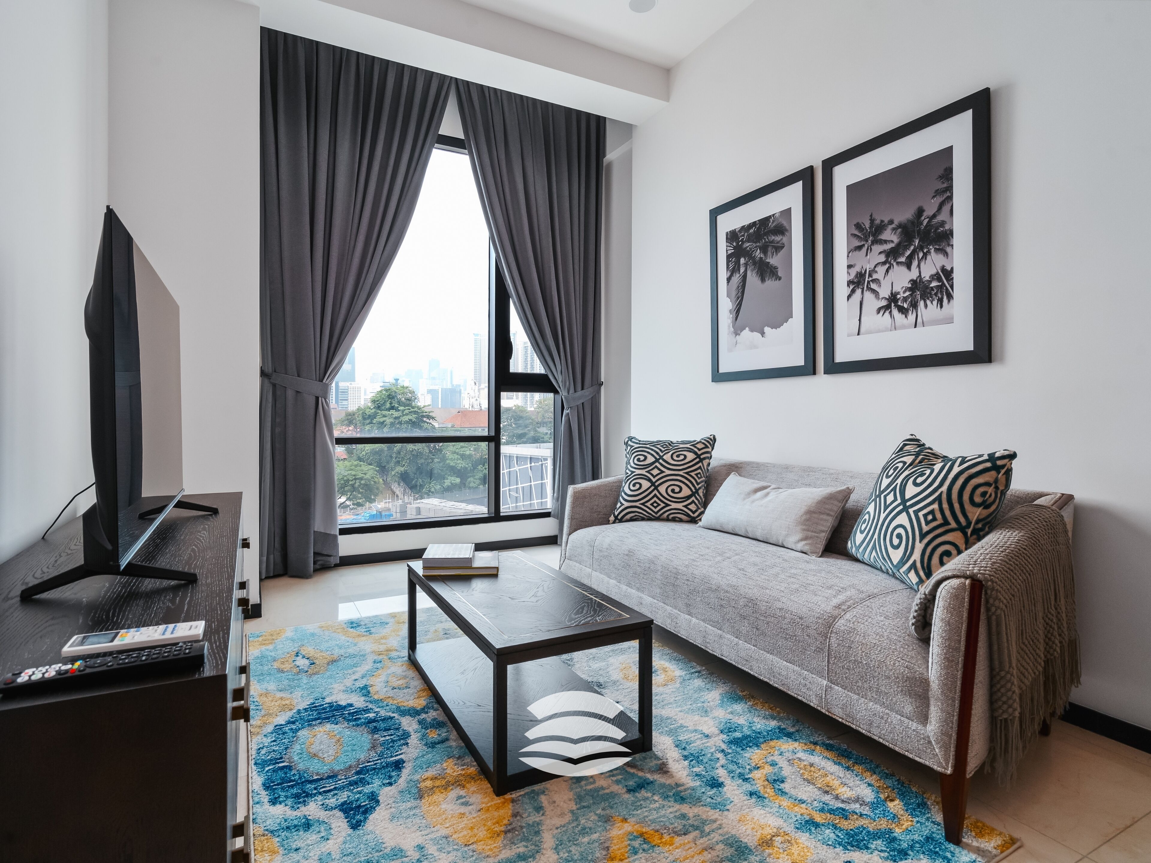 Un salon moderne avec un canapé, une table basse et un téléviseur, de grandes fenêtres avec des rideaux et deux tableaux encadrés accrochés au mur.