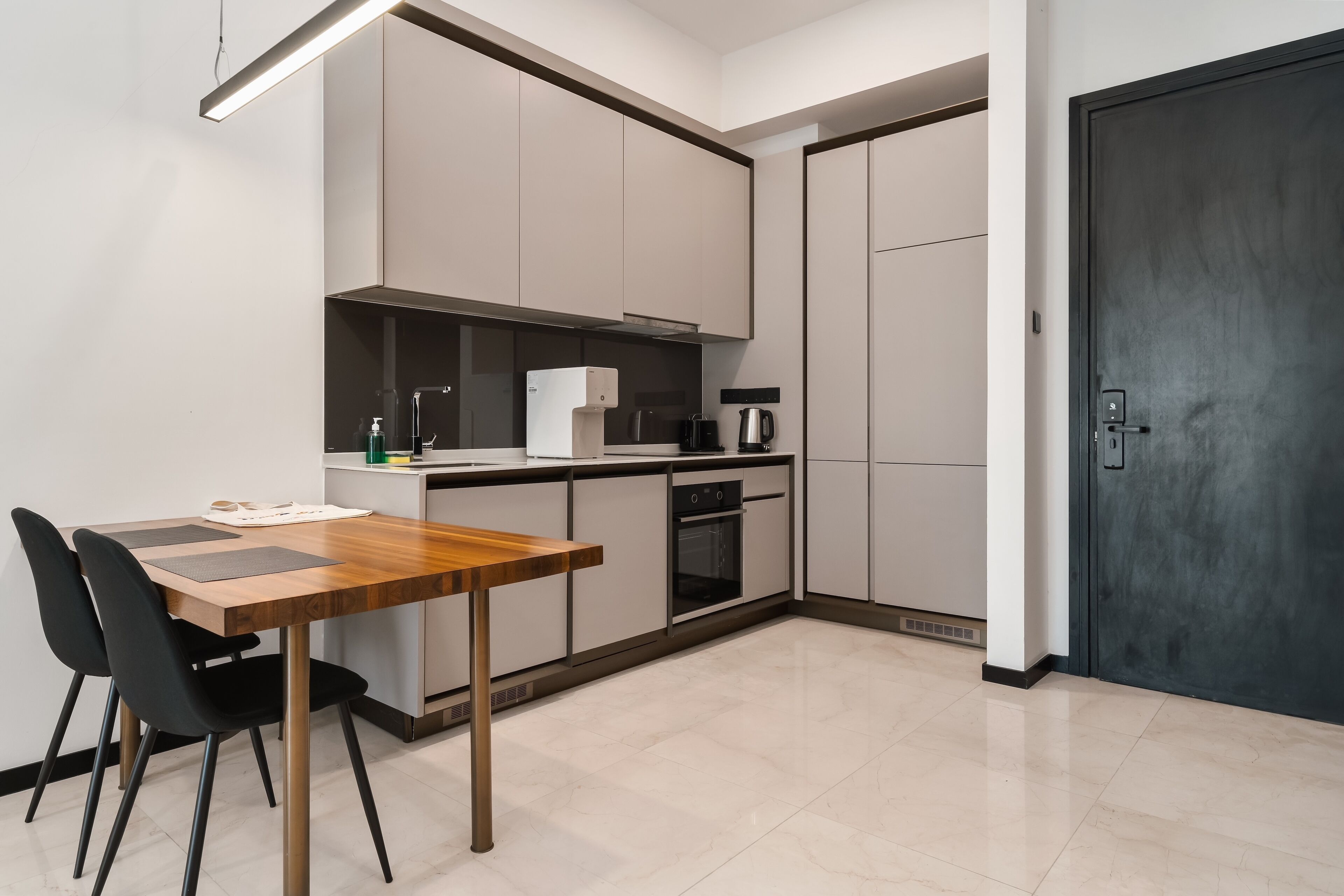 A modern kitchen with a wooden table and chairs, a coffee machine, and a black door.