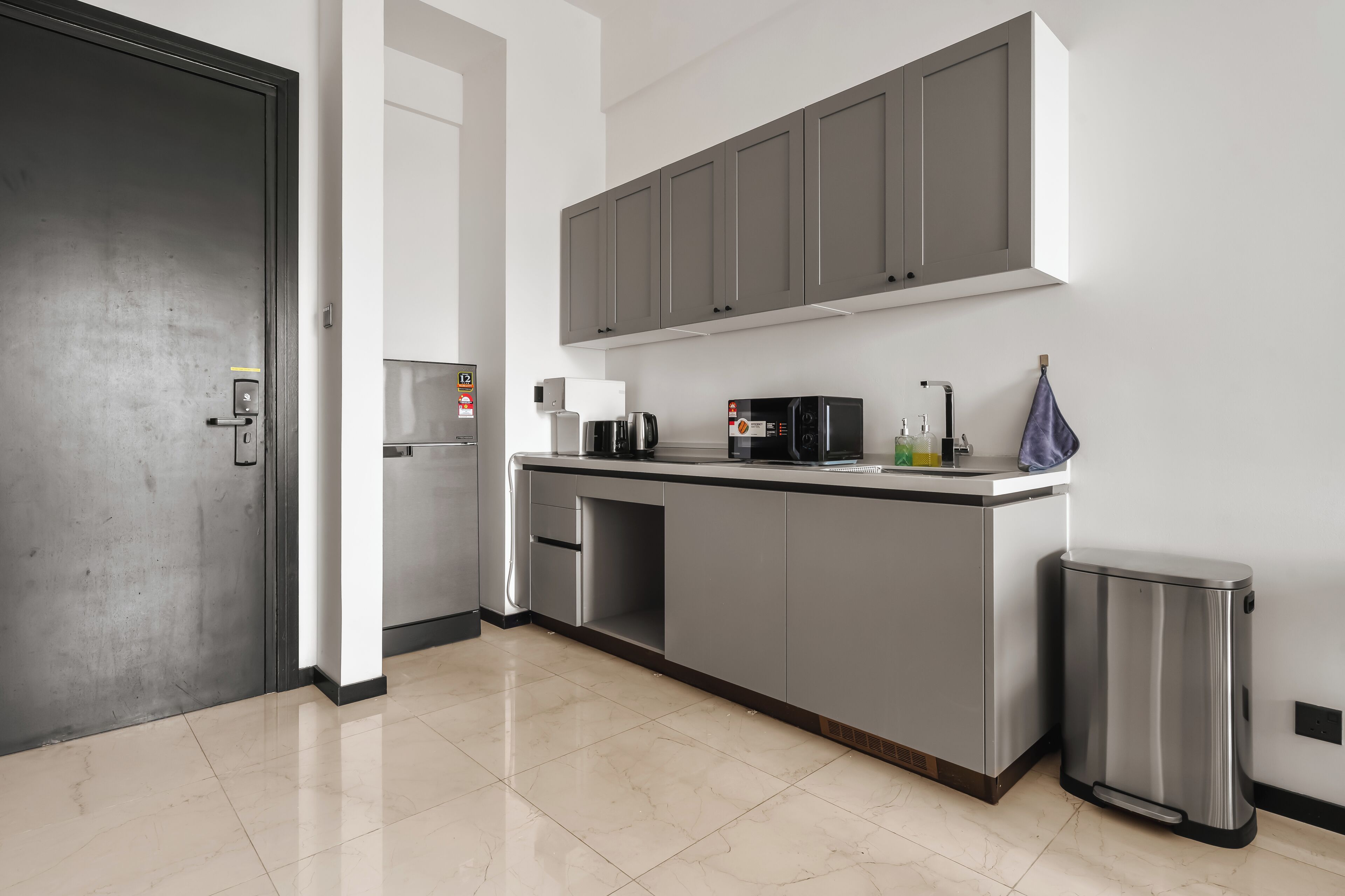 Une cuisine moderne avec des meubles gris, des appareils en acier inoxydable et un sol carrelé.