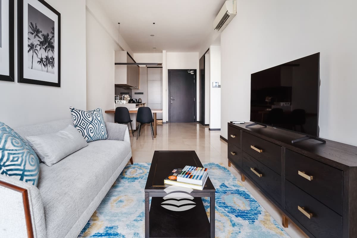 A modern living room with a sofa, coffee table, TV, and a kitchen in the background.