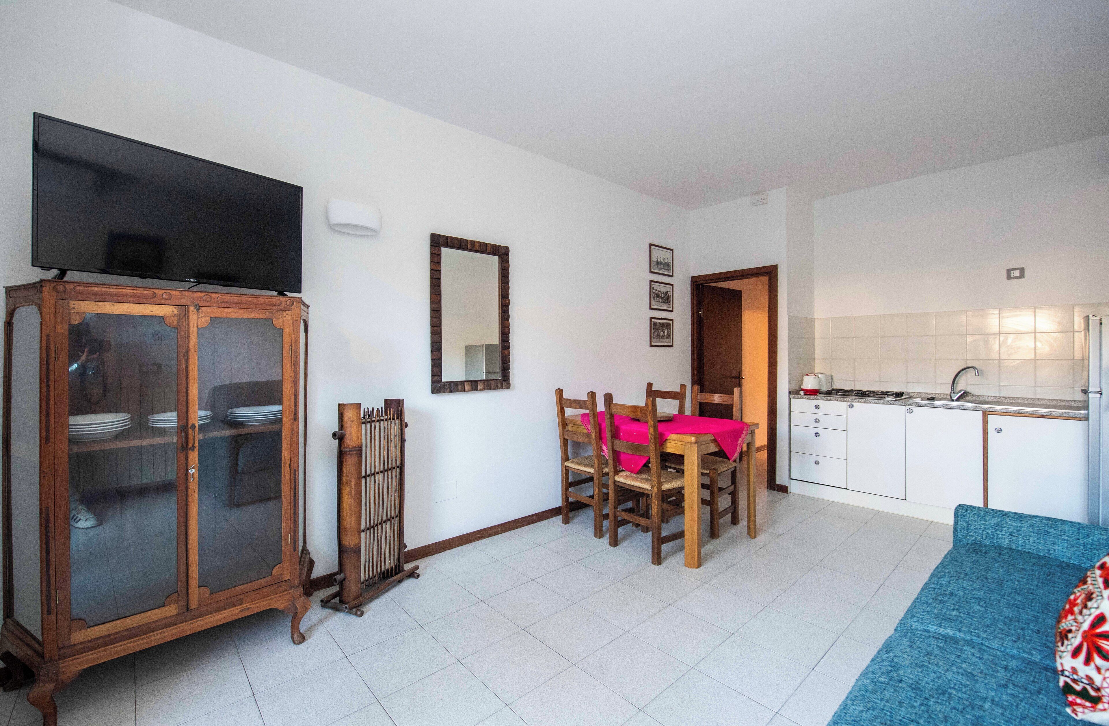 A compact living space with a dining area, kitchenette, and a television mounted on a cabinet.