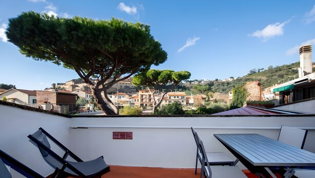 A terrace with a table and chairs, a tree, and a view of buildings in the distance. - LA TORRE Appartamenti (Castiglione della Pescaia)