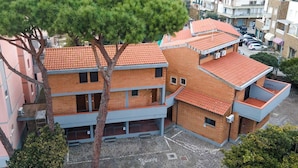 A multi-story building with a red-tiled roof, brick walls, and a central courtyard with a tree. - LA TORRE Appartamenti (Castiglione della Pescaia)