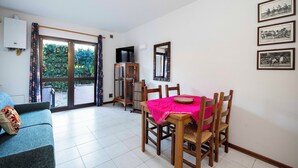 A room with a dining table, chairs, a sofa, a TV, and a window with curtains. - LA TORRE Appartamenti (Castiglione della Pescaia)