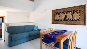 A living room with a teal sofa, a wooden dining table with blue cushions, and a wall-mounted decorative panel. - LA TORRE Appartamenti (Castiglione della Pescaia)