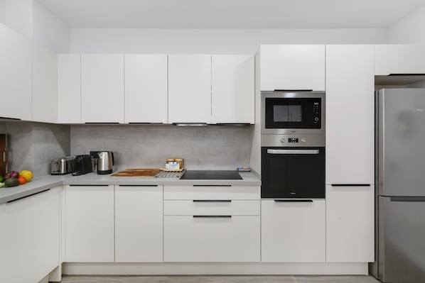 Una cocina moderna con armarios blancos, microondas, horno, tostadora y cafetera.