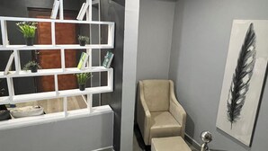 Een modern interieur met een grijze muur, een wit schap met planten, een beige fauteuil en een wenteltrap met metalen leuning.