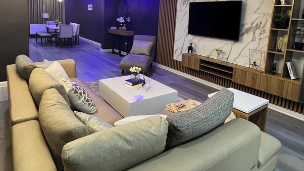 Een moderne woonkamer met een grote bank, een salontafel en een aan de muur bevestigde televisie.