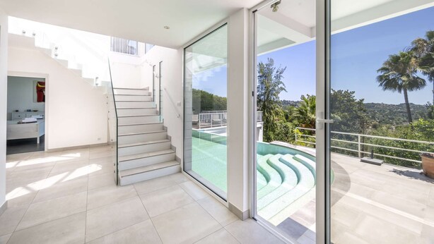 A modern interior with a staircase leading to a balcony overlooking a pool and greenery. - Villa Loupa - Calm and Harmony (La Colle-sur-Loup)