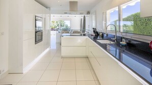 A modern kitchen with white cabinetry, a black countertop, and a large window offering a view of greenery. - Villa Loupa - Calm and Harmony (La Colle-sur-Loup)