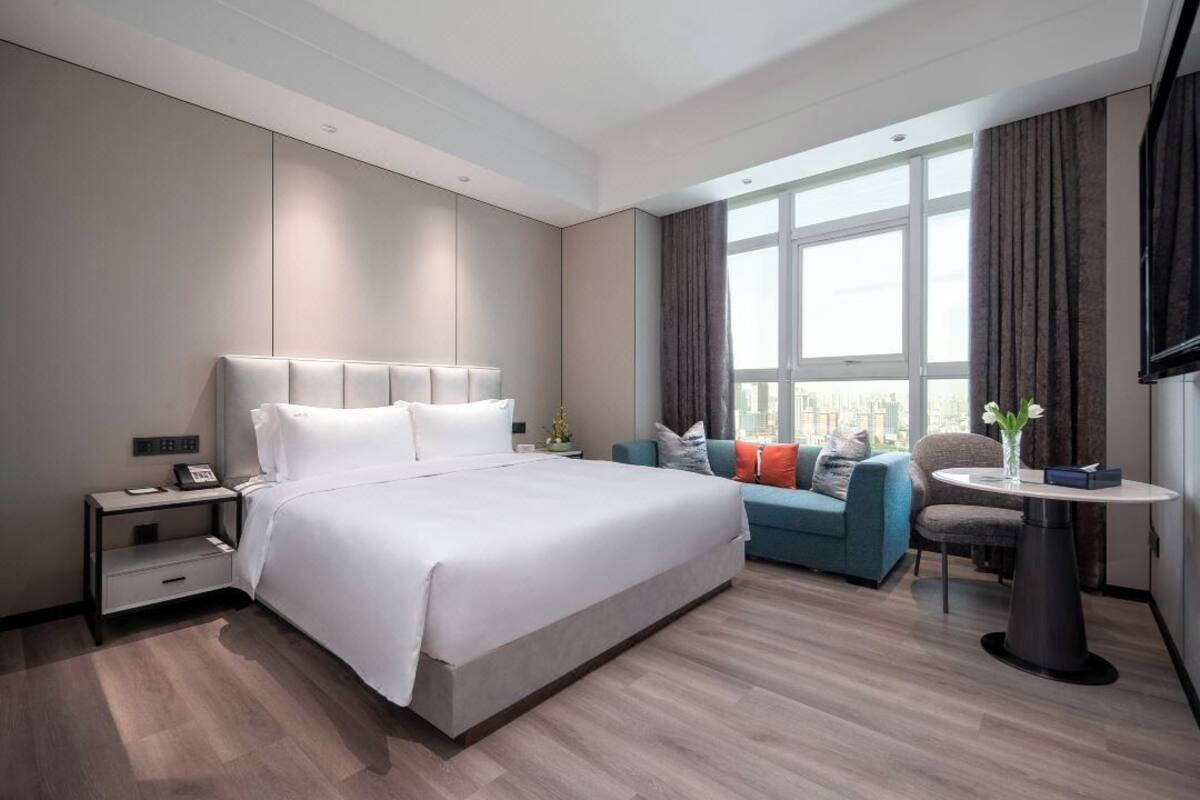 Une chambre d’hôtel moderne avec un grand lit, un canapé, une petite table et un téléviseur.