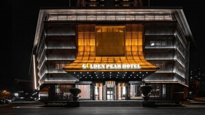 Exterior del hotel Golden Pear de noche, con un diseño arquitectónico moderno, una entrada destacada y señalización iluminada.