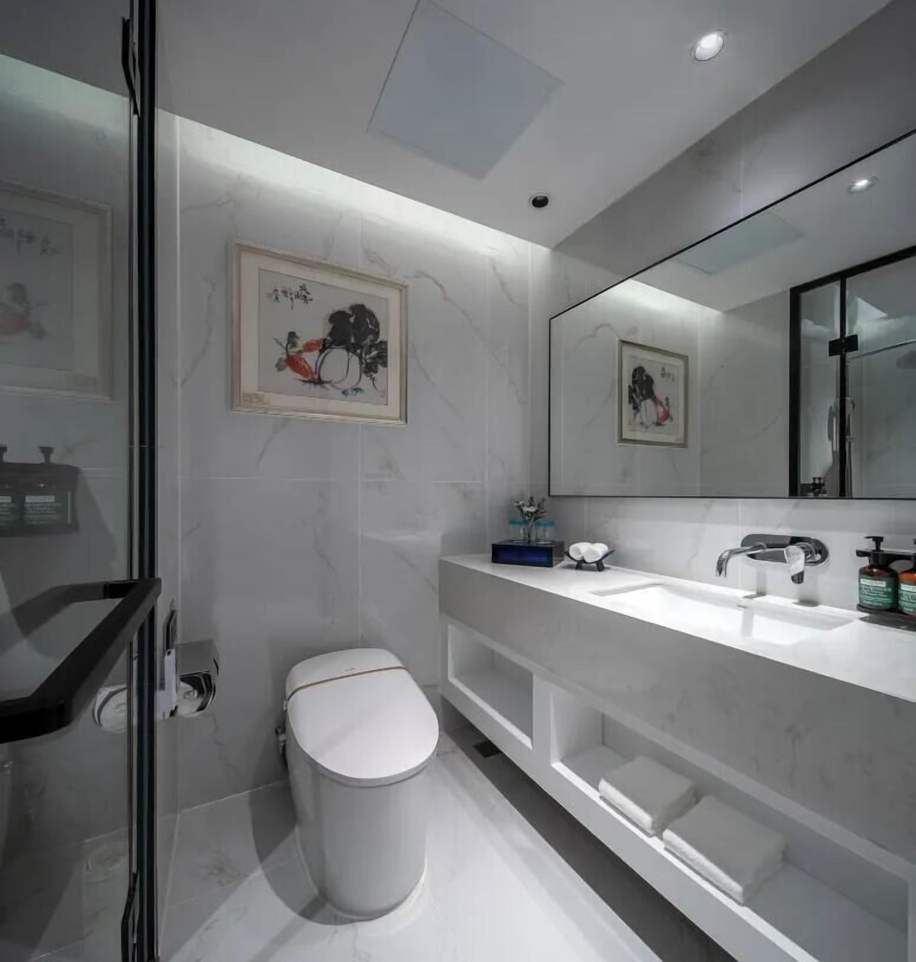 Une salle de bain moderne avec des toilettes, un lavabo et un grand miroir. Des œuvres d’art encadrées ornent le mur.
