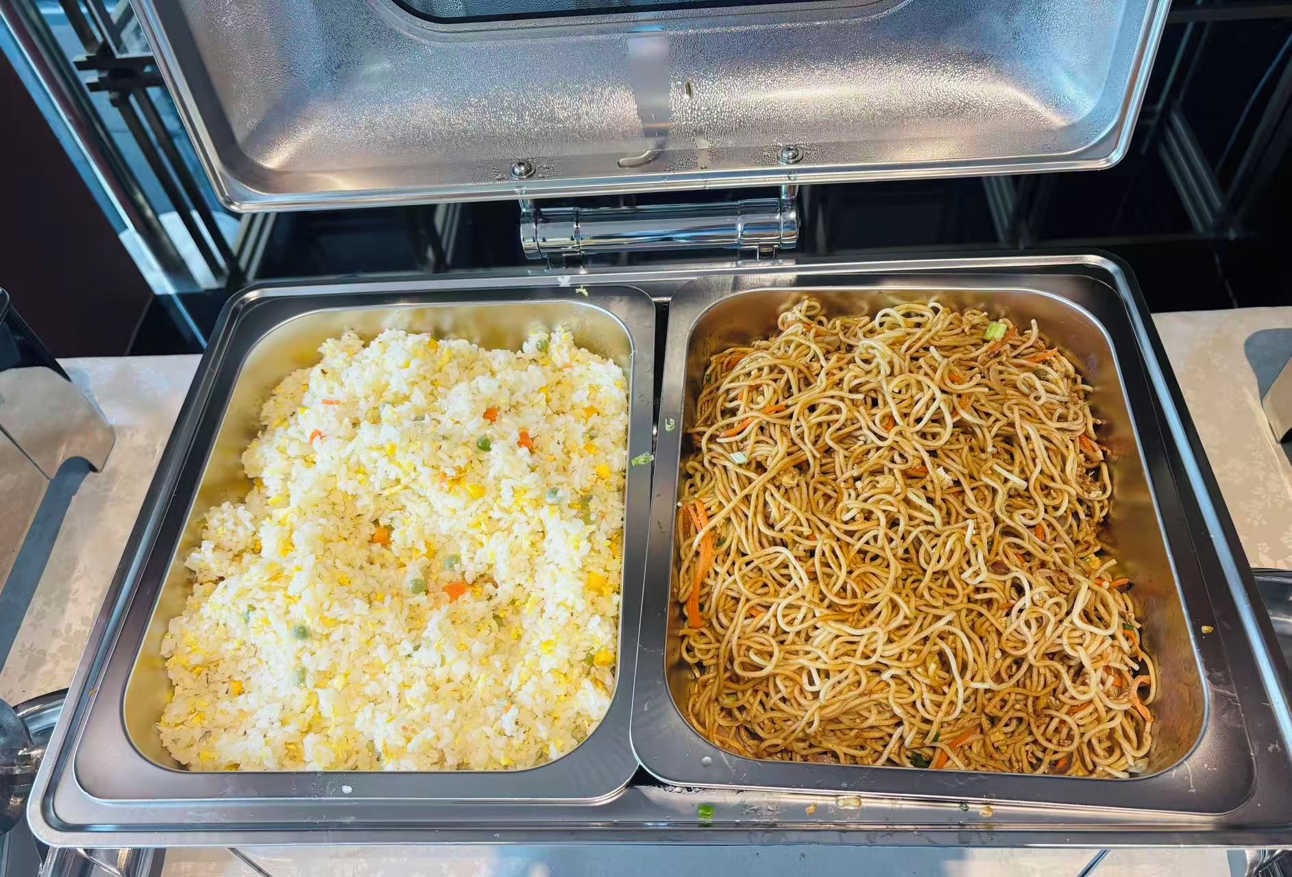 Un bufé con dos fuentes de comida, una de arroz frito y otra de fideos.