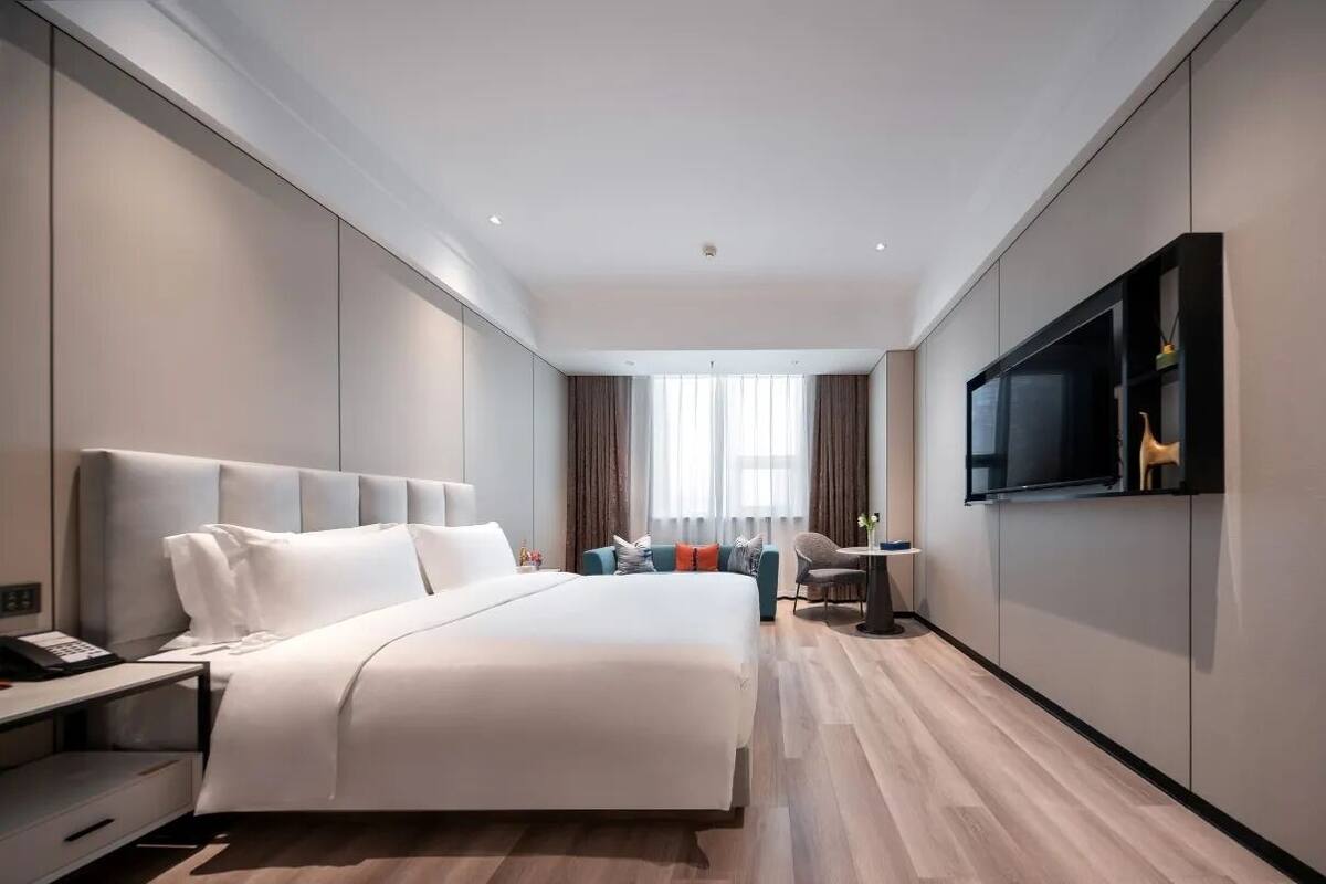 Une chambre d’hôtel moderne, dotée d’un grand lit, d’un bureau, d’une chaise, d’une télévision et d’une fenêtre avec des rideaux.