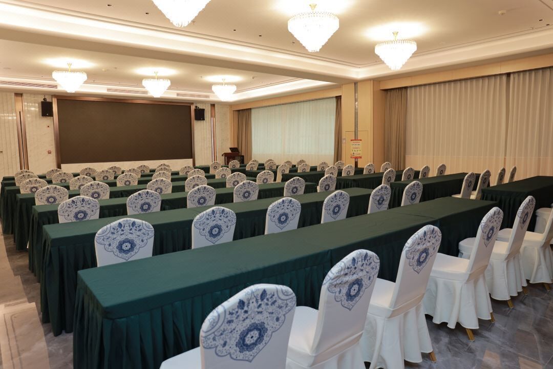 A conference room with rows of tables and chairs, a large screen, and a podium.