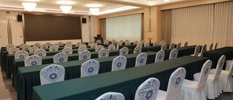 A conference room with rows of tables and chairs, a large screen, and a podium.