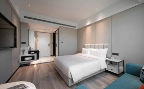 A modern hotel room with a large bed, bedside tables, a seating area, and a flat-screen TV. - Golden Pear Hotel (Wuxi)