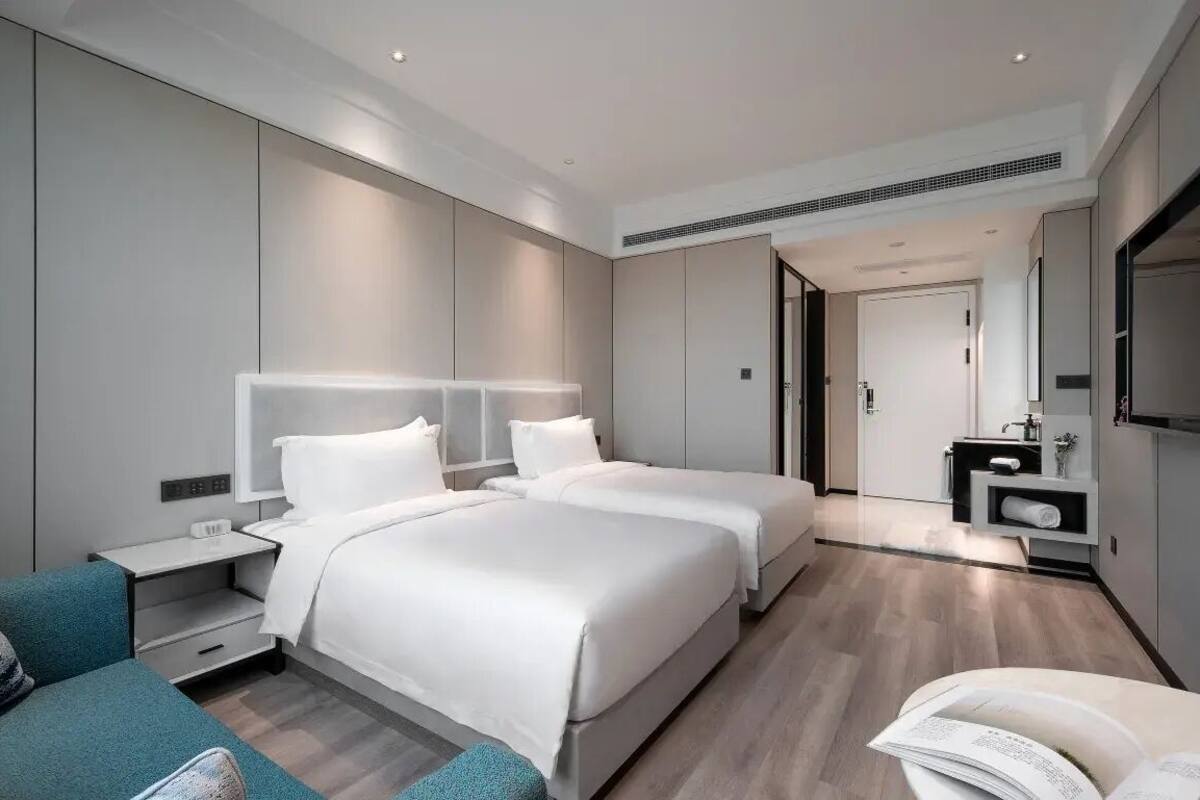 Une chambre d’hôtel moderne équipée de deux lits, d’un canapé, d’un bureau et d’une salle de bain avec un miroir et un lavabo.