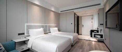 A modern hotel room with two beds, a sofa, a desk, and a bathroom with a mirror and sink.