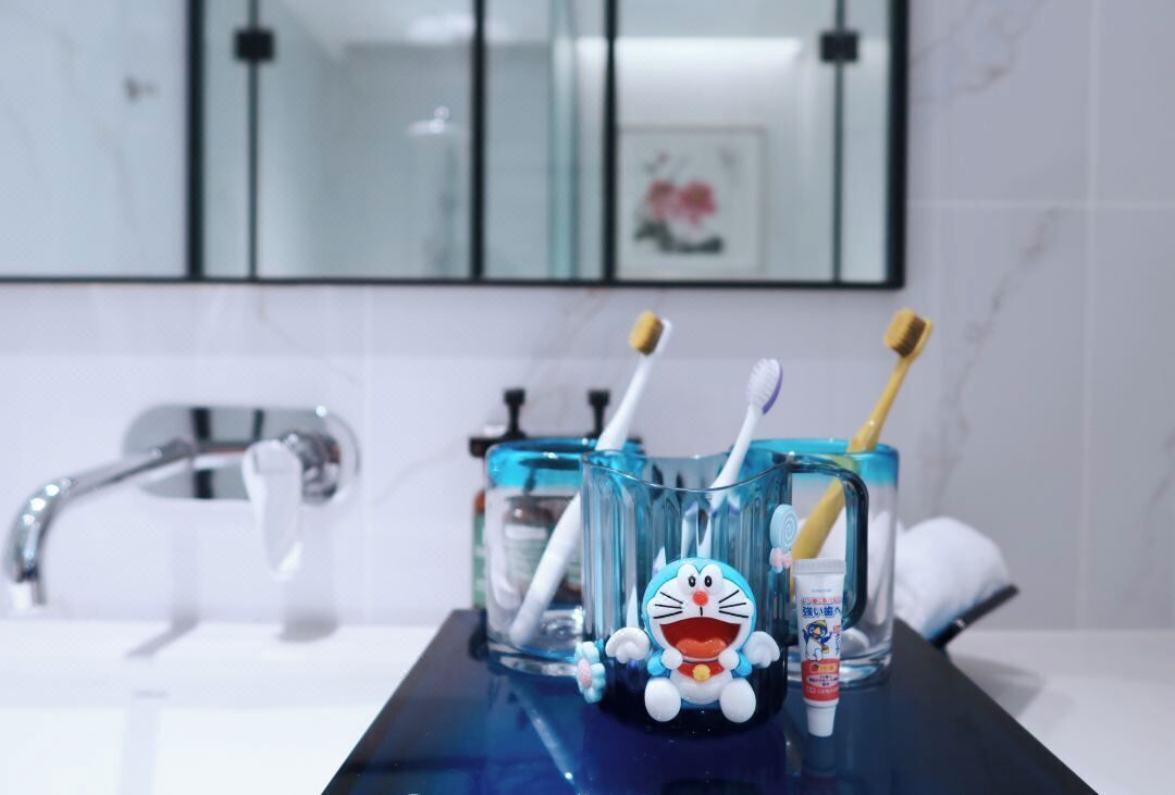 A bathroom with a sink, a mirror, and a glass container holding toothbrushes and a cartoon character.