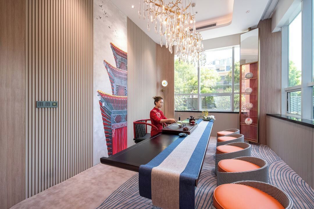 A modern room with a long table, cushioned seating, a decorative wall, and large windows.