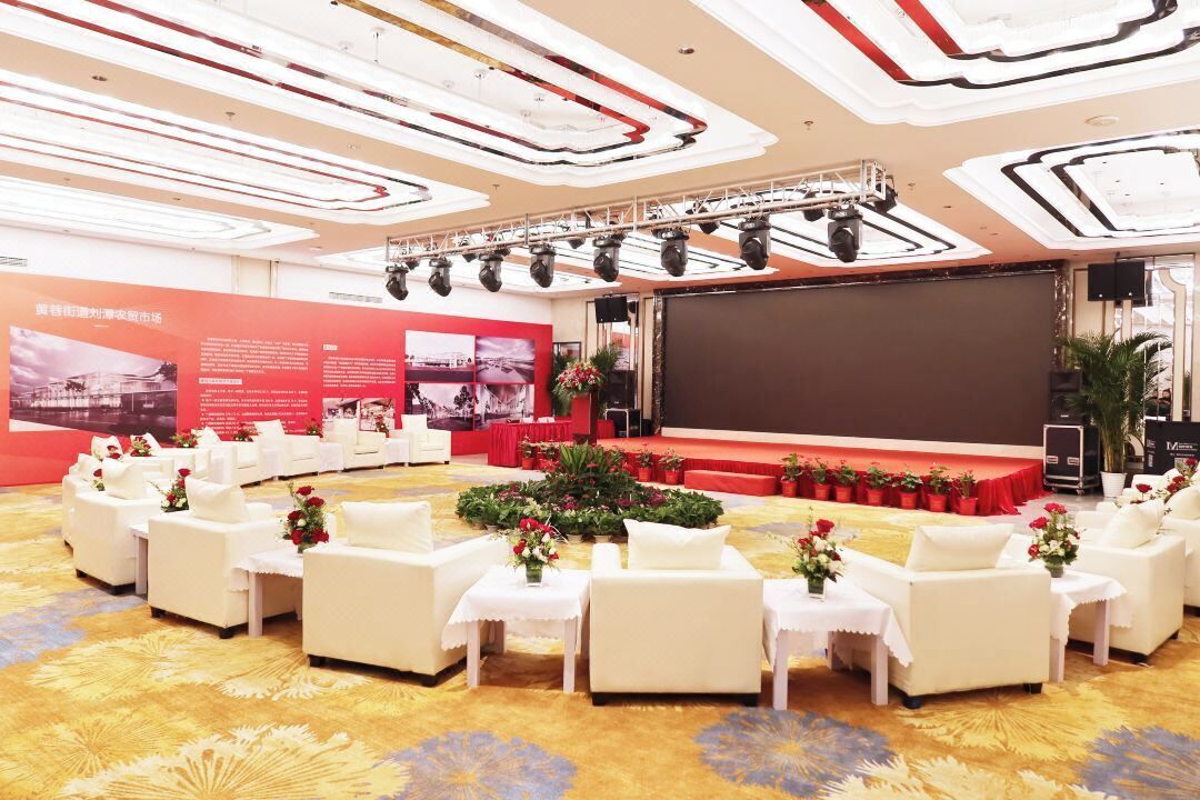 A conference room with a stage, white sofas, and a carpeted floor.