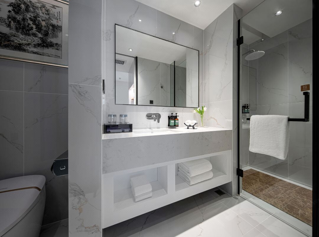 Un baño moderno con tocador de mármol, un espejo grande y cabina de ducha con mampara de vidrio.